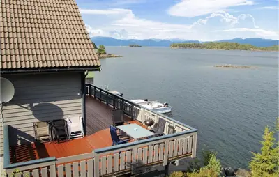 a house with a deck with a boat on the water at Galanten in Grimsland