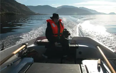 a man and a dog in a boat on the water at Cozy Apartment In Rosendal With Sauna in Rosendal