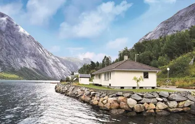 a house by the water with mountains in the background at Holiday Home Eidfjord Simadalsv in Eidfjord