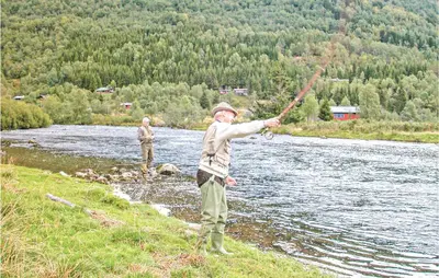 two people standing on the bank of a river fishing at Stunning Home In Sogndal With Sauna in Sogndal