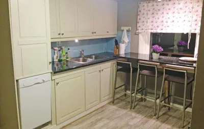 a kitchen with white cabinets and a sink and bar stools at Lovely Home In Vågstranda in Hjelvik