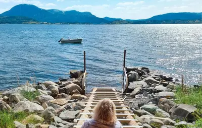 a person sitting on a dock looking at a boat in the water at Idavolden in Stangvik