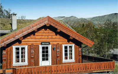 a wooden cabin with white windows and mountains in the background at Nice Home In Hemsedal With Sauna in Hemsedal