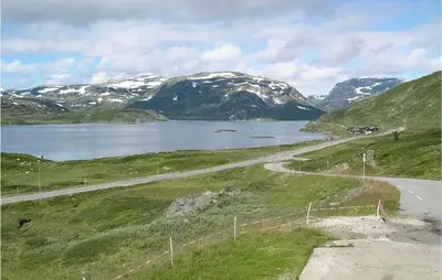 a road next to a lake with snow covered mountains at Holiday Home Vinje Skjærdalen