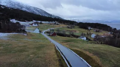 a road in the middle of a field with a mountain at Fjord side apartment in Jondal