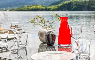a table with wine glasses and a red vase on it at Sjøbris in Erve