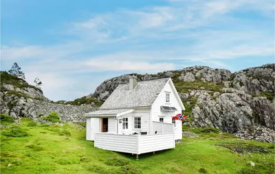 a small white house in a field with mountains at 2 Bedroom Cozy Home In Stolmen