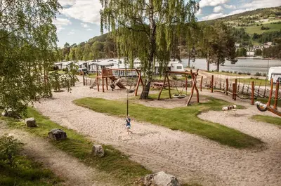 a child standing on a swing set in a playground at Fagernes Camping in Fagernes