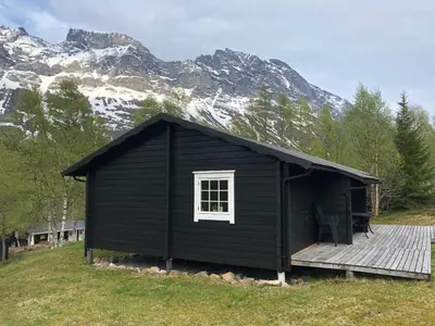 a black cabin with a deck in front of a mountain at Solvang World Heritage Camping in Eidsdal