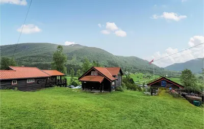 a group of buildings on a field with mountains in the background at 6 Bedroom Beautiful Home In Vossestrand in Vossestrand