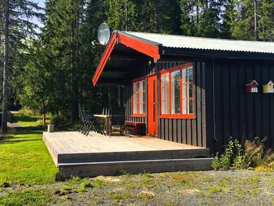 a small cabin with a deck and a table at Nærglimt - cabin by the lake Næra in Ringsaker