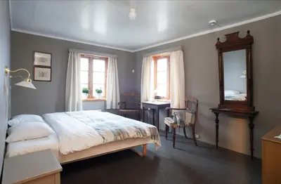 a bedroom with a bed and a desk and two windows at Glomstad Gjestehus in Tretten