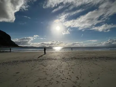 a person standing on a beach with the sun in the sky at Ytterland Apartments in Ålesund
