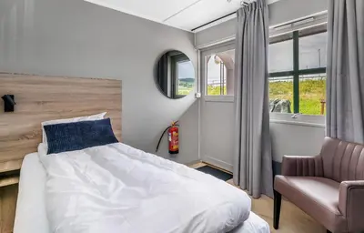 a bedroom with a bed and a chair and windows at Frich's Rudshøgda in Ringsaker