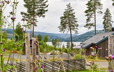 a wooden fence in front of a building with a lake at Cozy Home In Brøttum With Kitchen