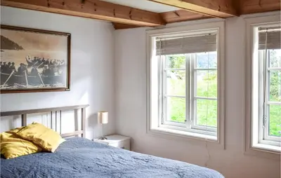 a bedroom with a blue bed and two windows at 2 Bedroom Cozy Home In Vallavik in Kaland
