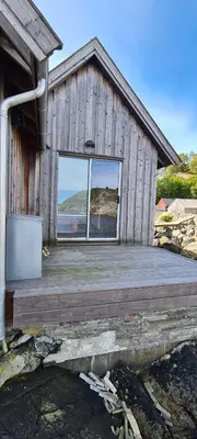 a wooden building with a large window on it at Exceptional Cottage 2 meters from the sea, possible to rent boat, Bekkjarvik, 60 km from Bergen in Gauksheim