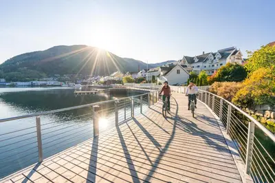 two people riding bikes on a bridge over a body of water at Hofslund Apartments in Sogndal
