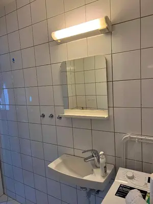 a white tiled bathroom with a sink and a mirror at Fløyen Apartment in Bergen
