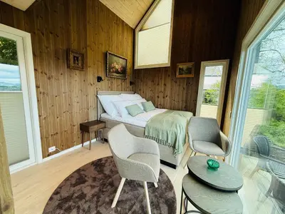 a bedroom with a bed and two chairs and windows at Kråen Gard in Larsnes