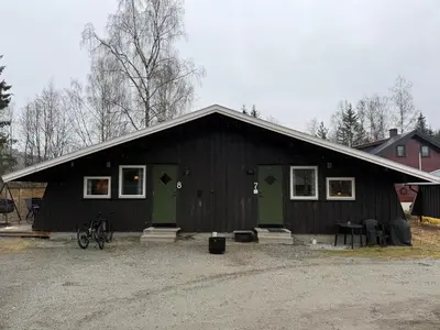 a black building with green doors and a bike in front at Koselig hytte med uteplas ved Hallingdalselva in Ål