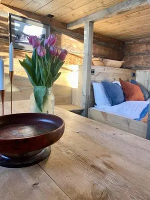 a wooden table with a vase of flowers and a bed at Sauefjøset - Idyllisk gardstun fra 1800-tallet in Skjåk