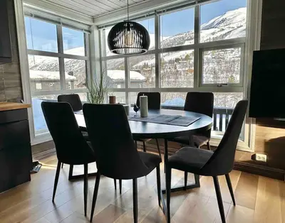 a dining room with a table and chairs and snow covered mountains at Lovise Mountain Apartment in Stranda